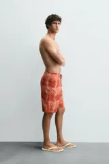 Short de baño color ladrillo con estampado de líneas curvas en color salmón. Tiene cintura elástica ajustable con cordón, bolsillos laterales y trasero.