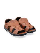 Sandalias de cuero color marrón con múltiples tiras entrecruzadas y ajuste con velcro. Suela de goma negra.