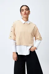 Remera blanca cropped de mangas cortas amplias con ojales metálicos a lo largo de las mangas.