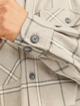 Sobrecamisa beige a cuadros con dos bolsillos frontales con botón, de manga larga y corte recto.