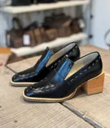 Mocasines negros de cuero con tacón de madera, puntera cuadrada y detalle de costuras en contraste.