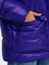 Campera puffer azul eléctrico con capucha, cierre frontal con cremallera, bolsillos laterales con solapa y puños con elástico. Diseño acolchado y corte holgado.