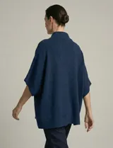 Capa o poncho tejido color verde esmeralda, con cuello polera alto que se cierra con un botón grande en el lateral. Presenta mangas cortas estilo japonesa y un calce amplio.