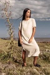 Vestido midi color crema, de corte recto y mangas cortas con puños elásticos. Presenta aberturas laterales en el ruedo.