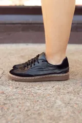 Zapatillas urbanas negras de cuero con puntera de gamuza, cordones negros y suela marrón.