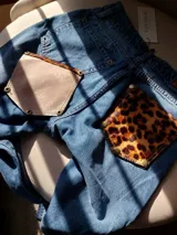 Pantalón de jean azul con bolsillos traseros desmontables con estampado animal print. Los bolsillos se sujetan al pantalón con remaches metálicos.