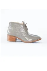 Botín gris de cuero charol brillante, con cordones frontales y tacón bloque de madera clara de 6 cm.