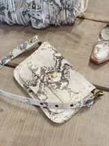 Bandolera con estampado de piel de serpiente en tonos blanco y negro, con correa ajustable y cierre metálico dorado.