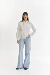 Camisa blanca de manga larga con cuello clásico y cierre frontal con botones. Presenta detalles de bordado calado a lo largo del frente.
