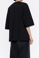 Camiseta negra de punto roma con escote en V pronunciado, manga corta y logo metálico pequeño en el frente.