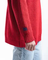 Sweater unisex de lana merino fina color rojo, con cuello redondo y corte relajado. Presenta un motivo inspirado en la técnica de zurcido visible.
