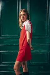 Vestido corto color rojo, con escote en V, sin mangas y dos bolsillos frontales. Se usa sobre una camisa blanca de mangas cortas con cuello clásico.