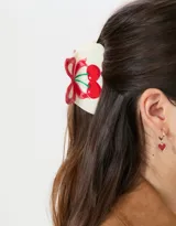 Broche para el pelo color crema con diseño de cerezas rojas y moño rojo.