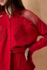 Camisa roja de lino con mangas largas, cuello camisero, cierre frontal con botones forrados y bordados florales. Presenta recortes de red calada en los hombros y bordados Millie en las mangas.