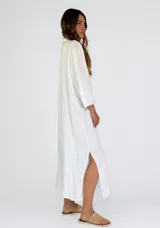 Vestido largo color beige de lino, con mangas largas abullonadas y volantes verticales en el frente. Cierre frontal con botones.