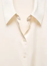 Camisa color crema de tejido fluido con textura y acabado satinado. Diseño recto, cuello clásico, manga larga con puños abotonados y cierre frontal con botones.