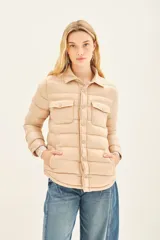 Campera puffer color beige con cuello camisero, cierre con botones a presión, bolsillos con solapa en el pecho y relleno de plumas.