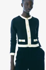 Saco corto negro de punto fino suave con cuello redondo, botones metálicos dorados y bolsillos insertados decorativos con botón adelante.