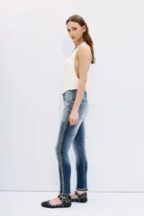 Jean de tiro medio-alto, calce slim loose, denim azul con desgaste localizado y bigotes. Galón de brillos en los laterales y ruedo desflecado.