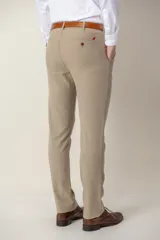 Pantalón de vestir color beige, de corte clásico, con bolsillos laterales y traseros. Se ajusta a la cintura con cinturón de cuero marrón.