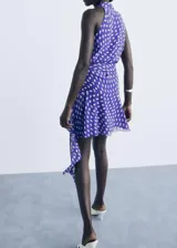 Vestido corto de poliéster, color azul con estampado de lunares blancos. Presenta cuello pico cruzado, tirantes anchos y diseño evasé con cierre lazo cruzado en la cintura.