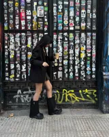 Bota negra de cuero ecológico con caña alta asimétrica y suela track con detalles metálicos.