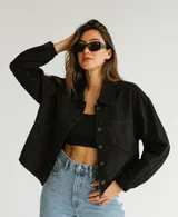 Campera negra de jean con corte cuadrado, cuello clásico, cierre frontal con botones metálicos, bolsillos de parche en el pecho y mangas largas con puños abotonados.