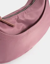 Bandolera hobo negra de tela deportiva con correa regulable, cierre superior, bolsillo frontal y charm lateral decorativo.
