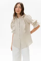 Camisa color beige de lino, con cuello redondo con mini volado, volado frontal que enmarca el pecho, y mangas 3/4 con volumen y puño elastizado.