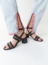Sandalias de gamuza negra con tiras translúcidas de TPU, taco redondo de 6 cm y tiras finas ajustables al tobillo. Cuentan con forro y plantilla de cuero y suela de goma.