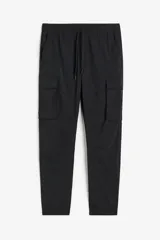 Pantalón jogger negro de nylon elastizado, corte slim fit, con cintura elastizada ajustable con cordón, bolsillos laterales, bolsillos cargo con solapa y botón a presión, bolsillos traseros y bajos elastizados.