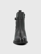 Bota corta de cuero negro con caña media, detalle de tira con hebilla metálica en el tobillo y elástico lateral. Cuenta con suela plana y taco bajo cuadrado.