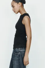 Camiseta ajustada (slim fit) de cuello redondo y manga sisa, color beige claro, con frunces laterales y bajo asimétrico con terminación de encaje a tono.