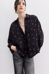 Camisa fluida negra con estampado de corazones color lila, mangas largas, cuello camisero y puños con botón.