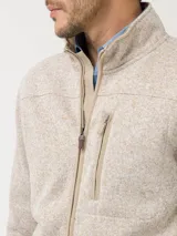 Campera polar color beige jaspeado, con cuello alto, cierre frontal completo y bolsillo vertical con cierre en el pecho.