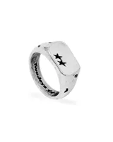 Anillo tipo sello de plata 925 con acabado oxidado. La parte superior rectangular presenta dos estrellas negras grabadas. El interior del aro lleva el nombre de la marca grabado.
