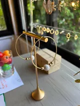 Aros de oro con forma de aro, con una piedra volcánica blanca y pequeñas cuentas doradas.