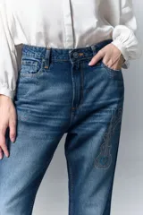 Jean de tiro alto y calce recto, confeccionado en denim azul rígido. Presenta un diseño de hotfix brillante en forma de guitarra en el frente de la pierna derecha.