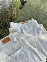 Pantalón de lino color beige con estampado de pequeñas flores blancas y rojas.