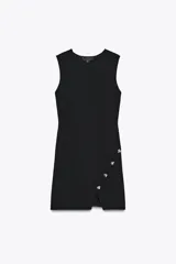 Vestido corto negro de punto, con cuello redondo y sin mangas. Tiene una abertura en el ruedo y detalle de botones metálicos irregulares cruzados en el lateral.