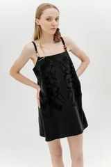 Vestido corto negro con bordado floral, breteles finos y detalle de cuentas de madera.