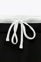 Pantalón negro de tiro alto con doble cintura elástica ajustable con cordón y tejido combinado. Pinzas frontales, bolsillos delanteros y falso bolsillo de vivo en espalda. Pernera ancha.