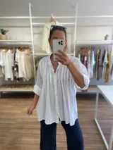 Camisa de algodón color amarillo con diseño de línea italiana, corte holgado y asimétrico. Presenta cuello camisero, cierre frontal con botones y detalle de pliegues verticales en el pecho. Cuenta con mangas largas y puños con botón.