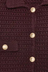 Chaqueta de punto color borgoña, con cuello camisero y manga larga. Tiene falsos bolsillos con solapa en el delantero y cierre frontal con botones metálicos dorados.