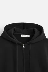 Sudadera negra relaxed fit de algodón compacto con interior en rizo, cuello con capucha ajustable, manga larga, bolsillos frontales tipo canguro, acabados en rib y cierre frontal con cremallera.