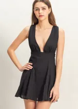 Vestido corto negro con escote en V pronunciado, sin mangas y falda acampanada.