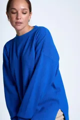 Sweater color beige de tejido de punto acanalado, con cuello redondo y mangas largas. Tiene corte holgado y aberturas laterales en el ruedo.