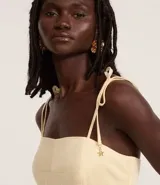 Vestido midi color amarillo pálido, con escote recto y busto con recortes. Posee breteles finos ajustables con lazo y cierre trasero de cremallera.