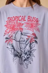 Remera blanca de algodón con estampado de un tucán, palmeras y la frase 'Tropical Bliss' en tonos naranja y rosa.