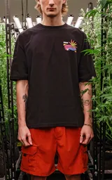 Remera negra de corte oversize con hombros caídos y cuello redondo. Estampado en la espalda con tres imágenes rectangulares apiladas y una ilustración de un sol con plantas de cannabis.